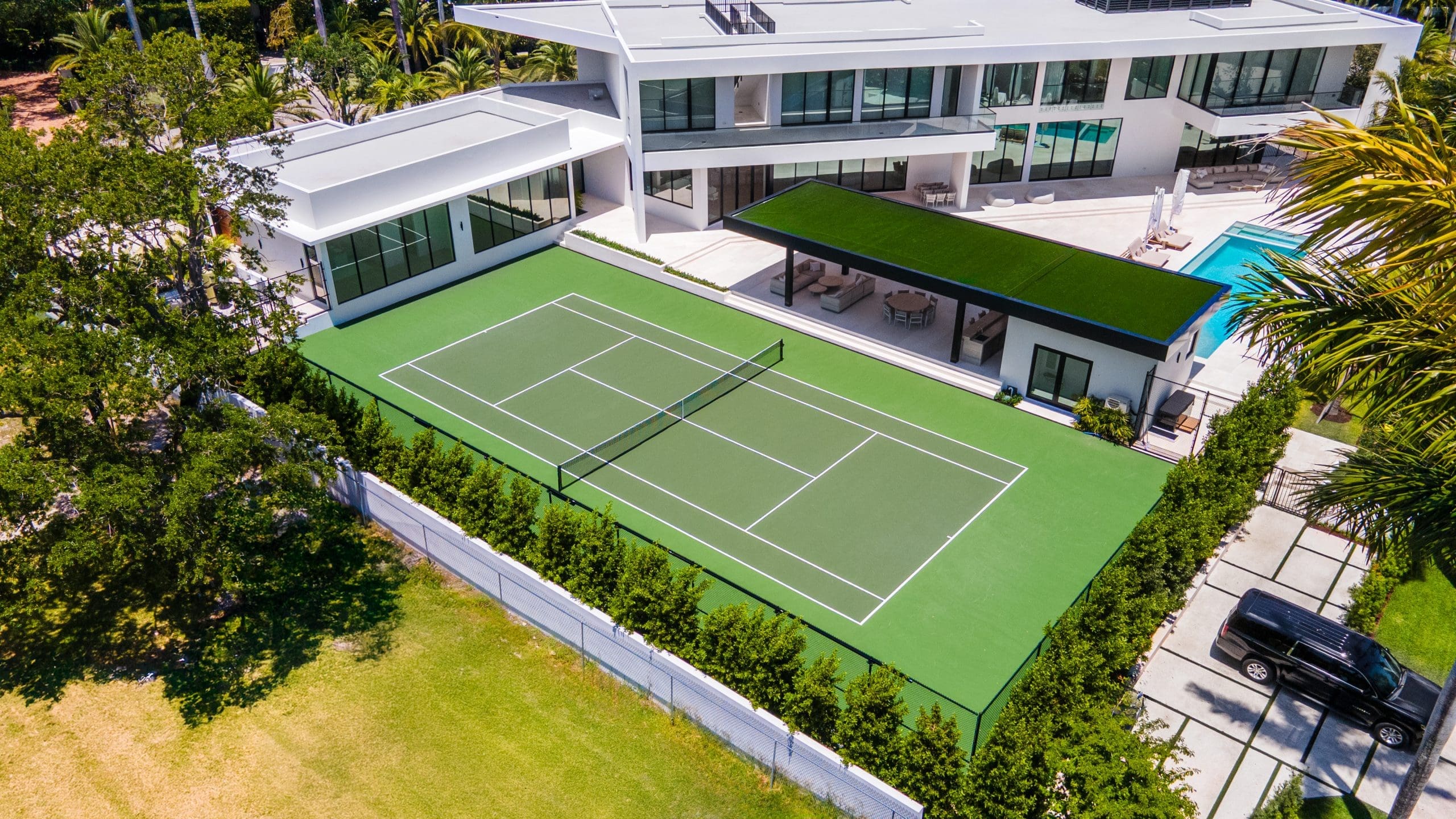 Aerial view of a green private tennis court beside a modern white residence