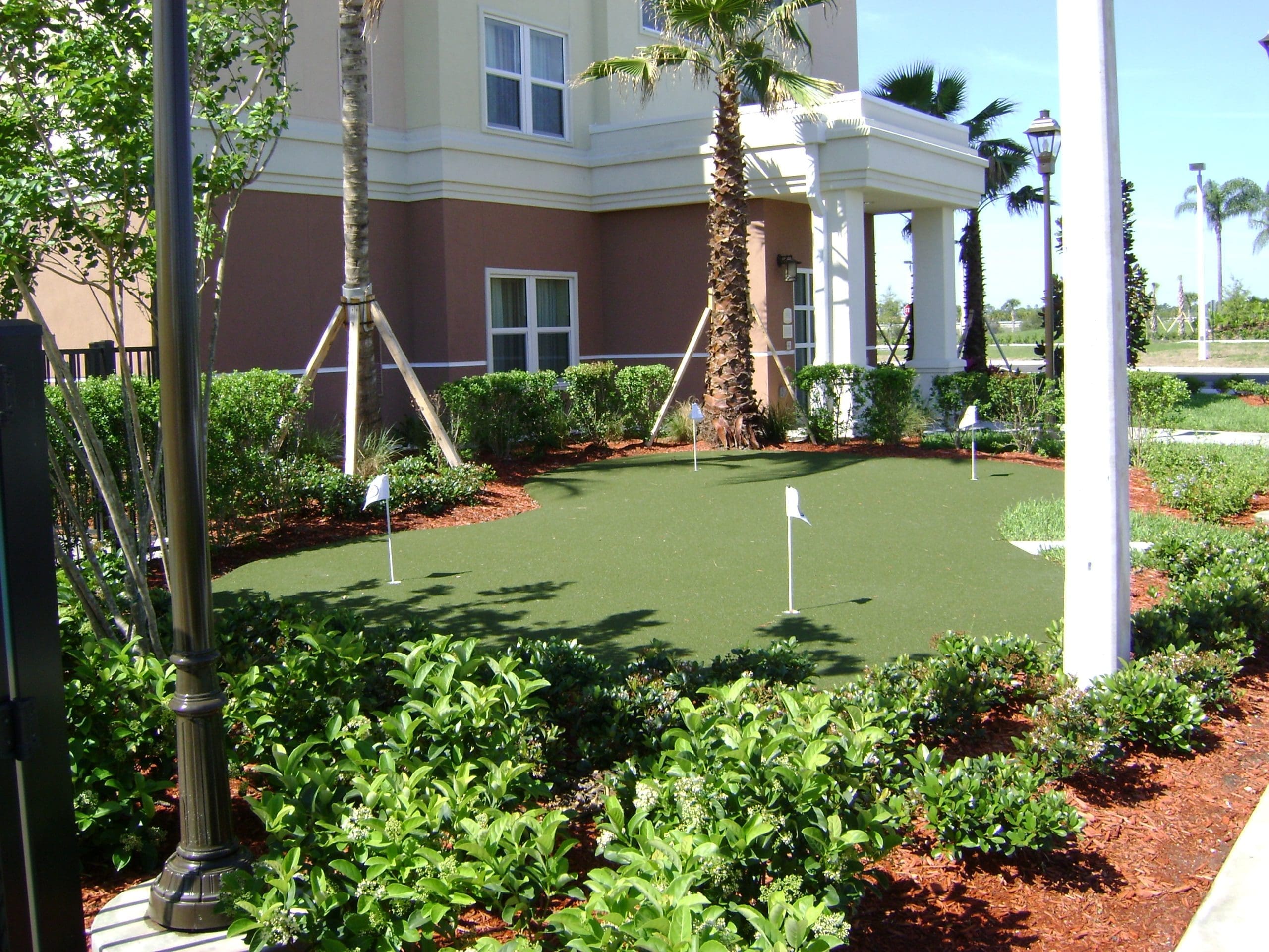 Small artificial putting green beside a residential building and tropical landscaping