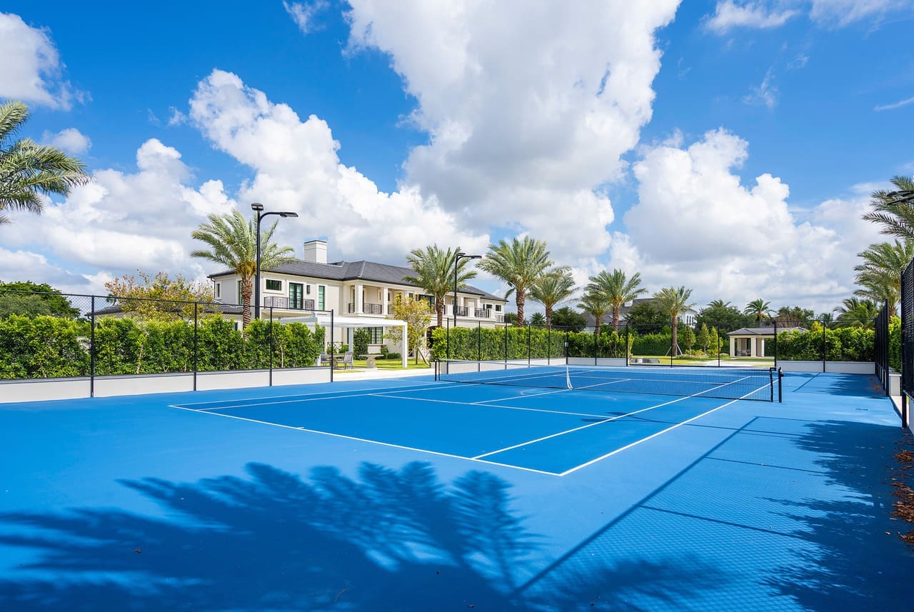 Bright blue outdoor tennis courts with white lines, palm trees and nearby homes