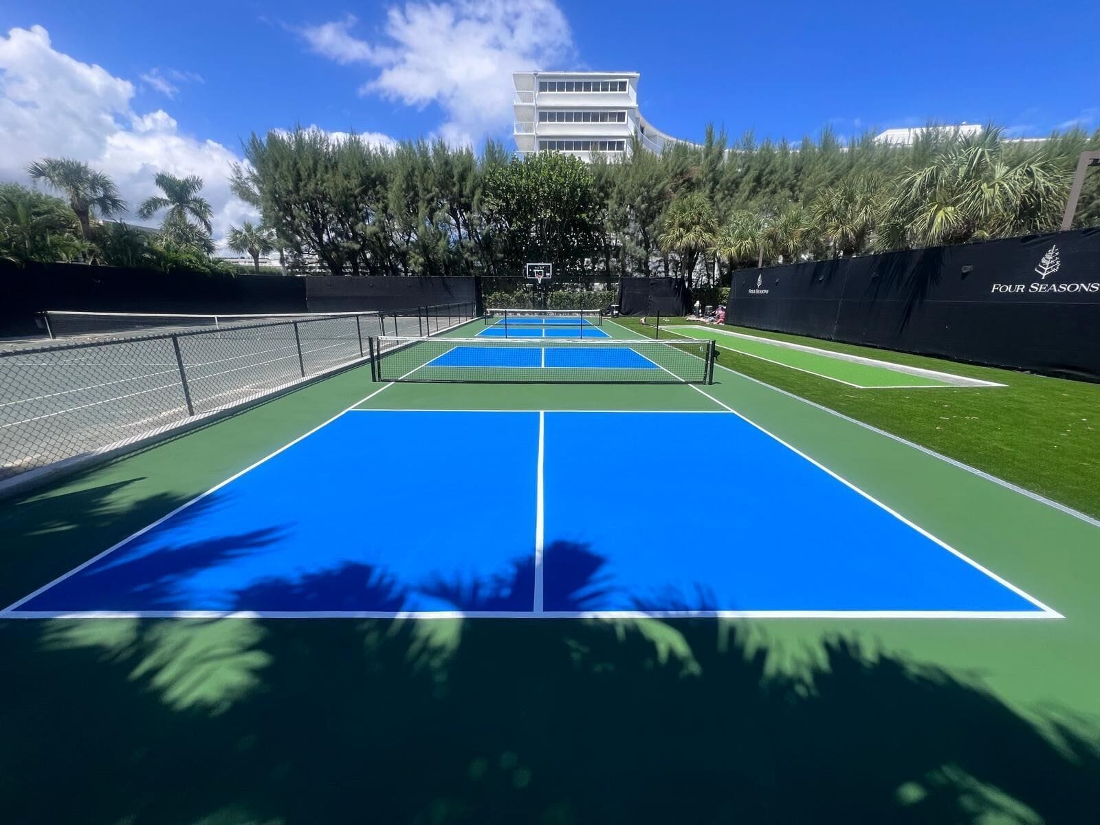 Two blue outdoor pickleball courts with green surrounds and white lines