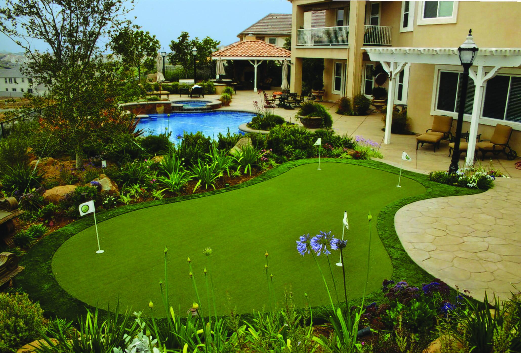 Residential backyard putting green beside a swimming pool and landscaped home