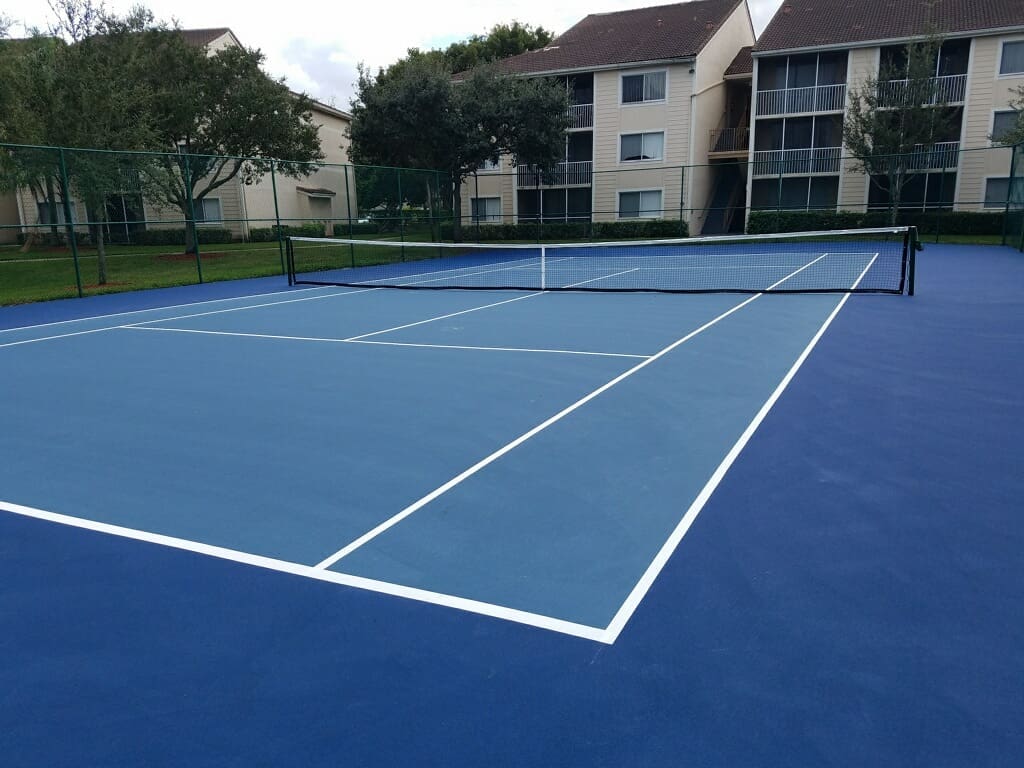 Blue outdoor tennis court with white lines near residential buildings