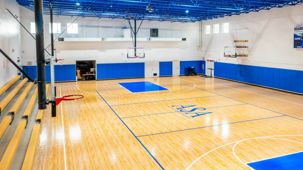Indoor school gym with polished wood basketball flooring, blue accents, and wall-mounted hoops