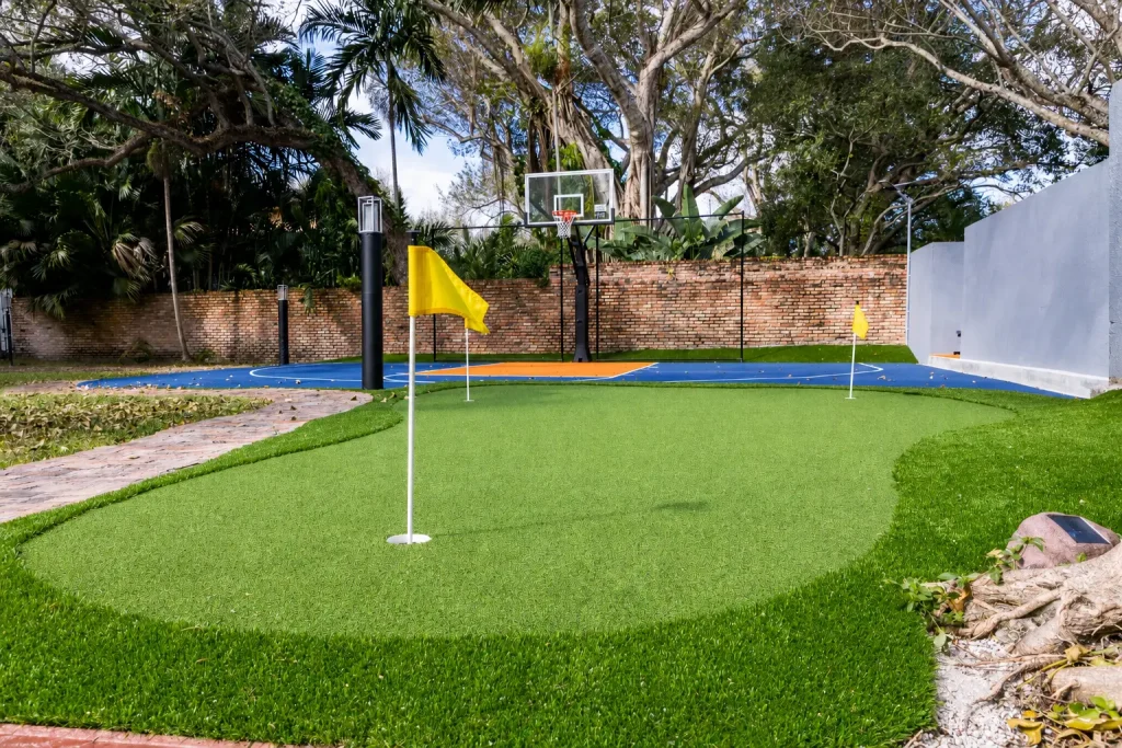 Backyard artificial turf putting green with yellow flags and a blue and orange basketball court behind it