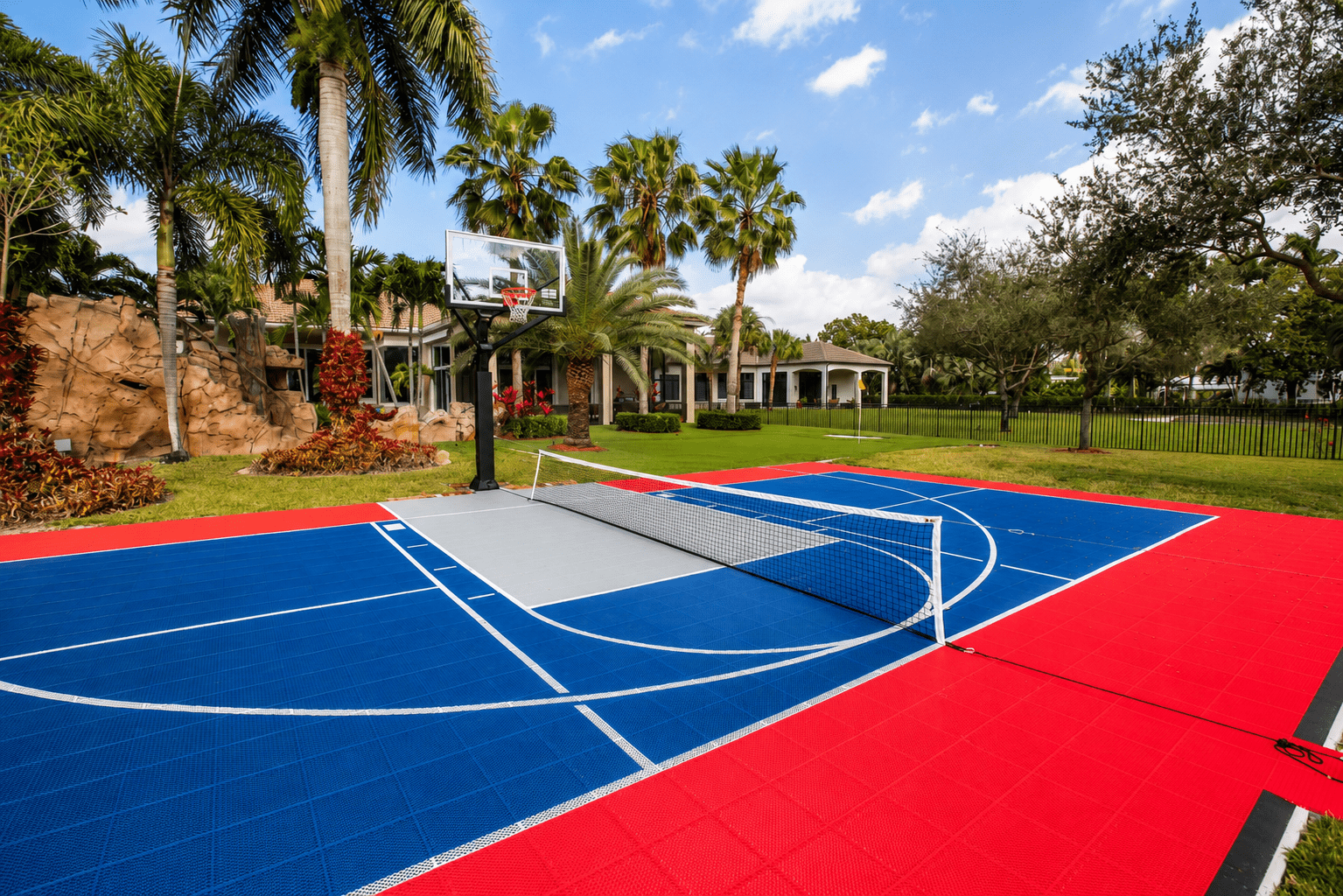 Custom red and blue backyard basketball court surrounded by palm trees